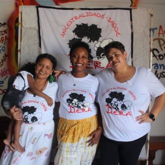 Três mulheres e uma criança no colo lado-a-lado, uniformizadas com a camisa do Ilera sorrindo.